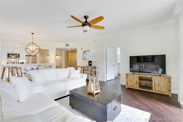 A living room features a white sectional sofa, a dark wooden trunk coffee table, and a television — 100 Uno Lago Drive # 205, Juno Beach FL 33408, JUNO BEACH, FL