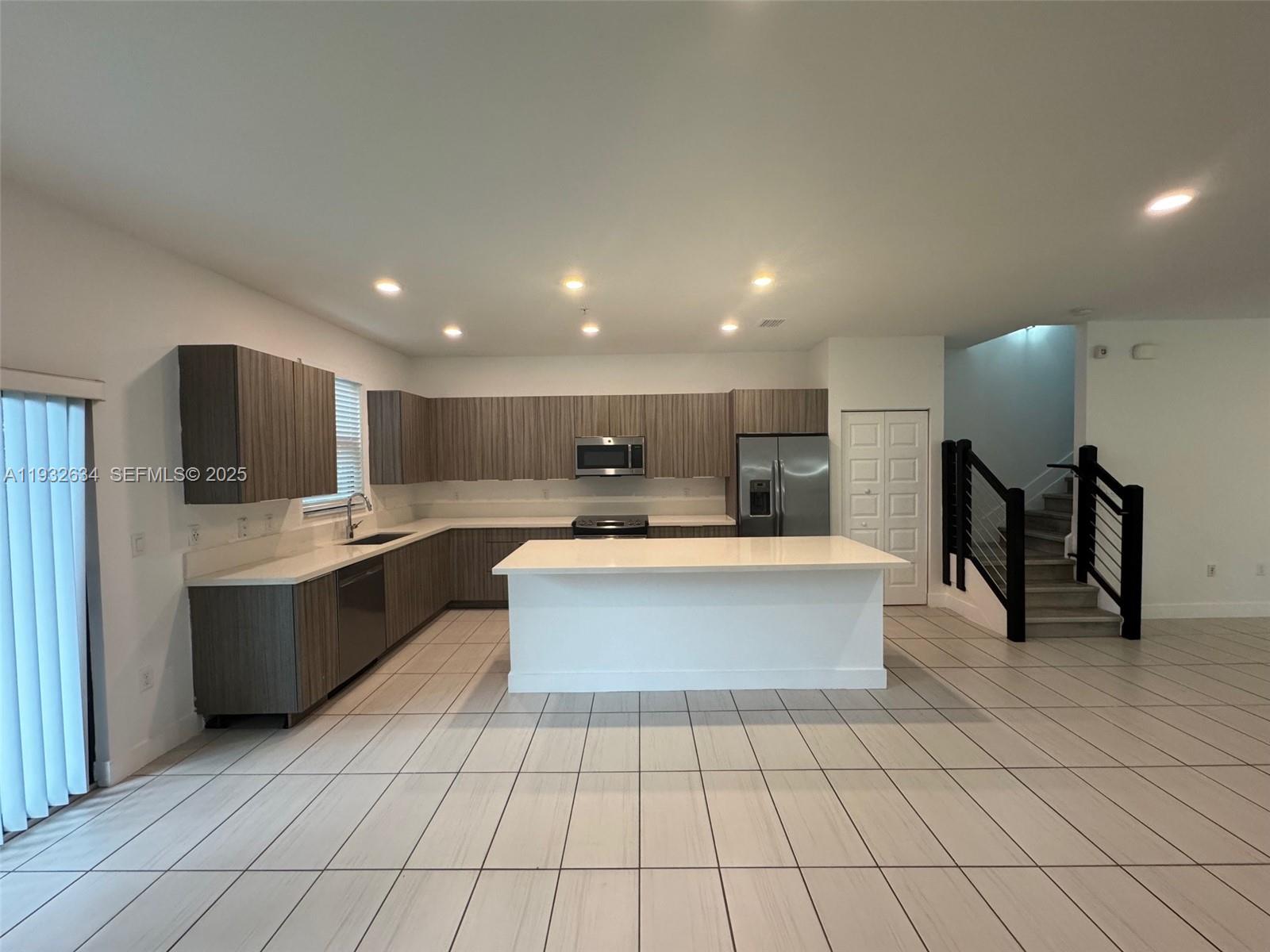 A modern kitchen features wood-grain cabinets, white countertops, a central island, and tiled flooring — 10461 NW 82nd St # 6, Doral FL 33178, DORAL, FL