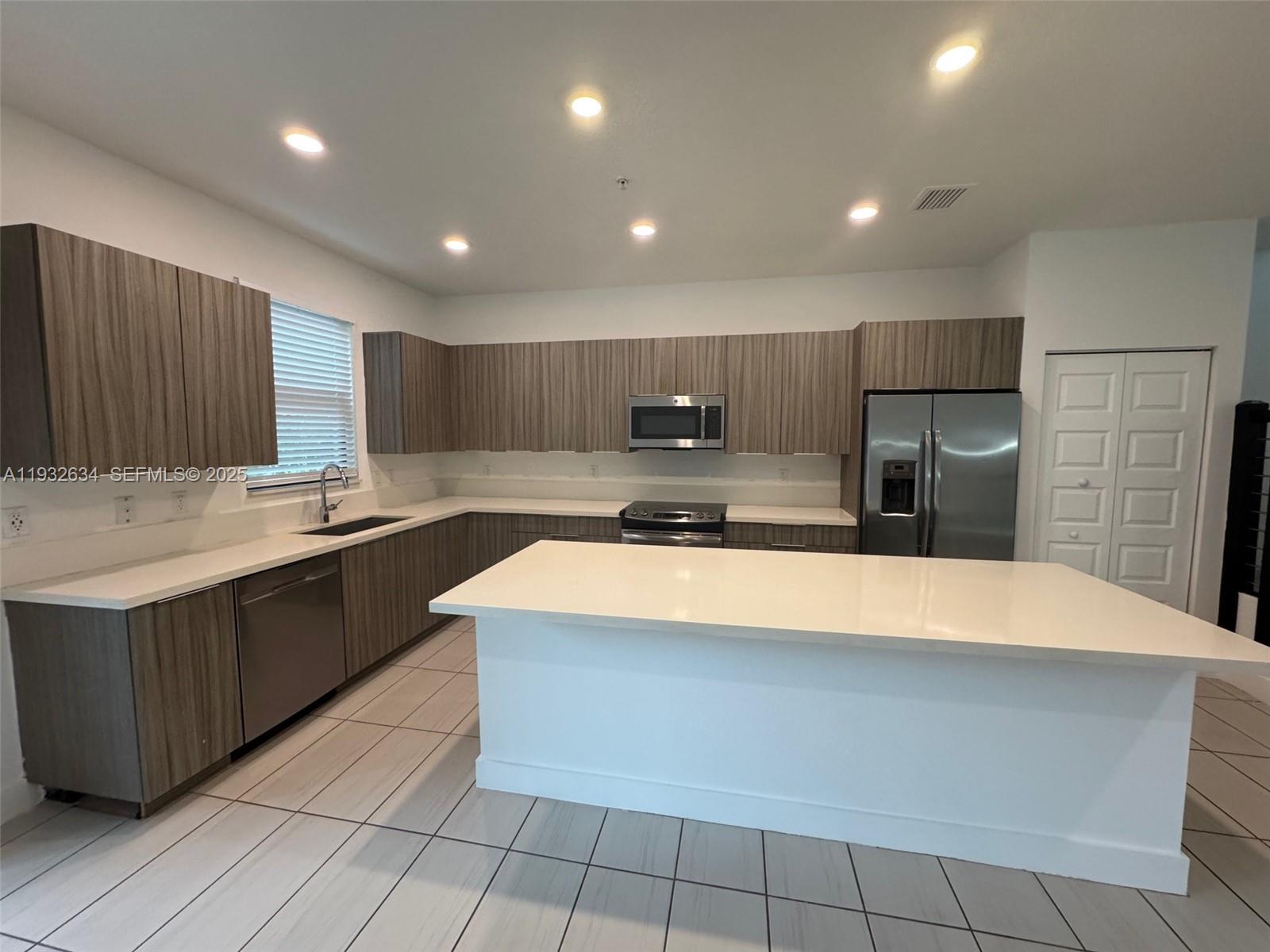 A kitchen features wood-grain cabinets, white countertops, stainless steel appliances, and light-colored tile flooring — 10461 NW 82nd St # 6, Doral FL 33178, DORAL, FL