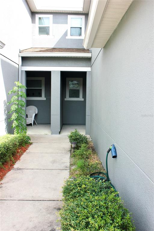 A concrete walkway leads to two recessed entryways with windows on a gray stucco building — 1017 CHALCEDONY STREET, KISSIMMEE, FL