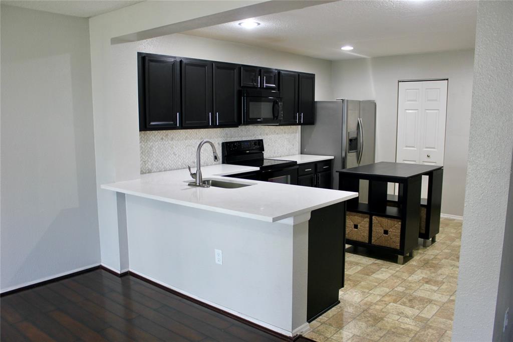 A kitchen features black cabinets, white countertops, stainless steel appliances, and a small island — 1017 CHALCEDONY STREET, KISSIMMEE, FL