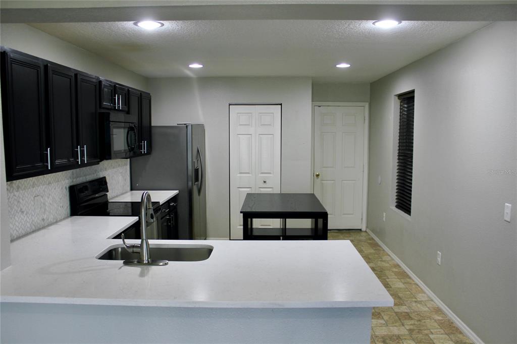 A kitchen features black cabinets, white countertops, stainless steel appliances, and a small black island — 1017 CHALCEDONY STREET, KISSIMMEE, FL