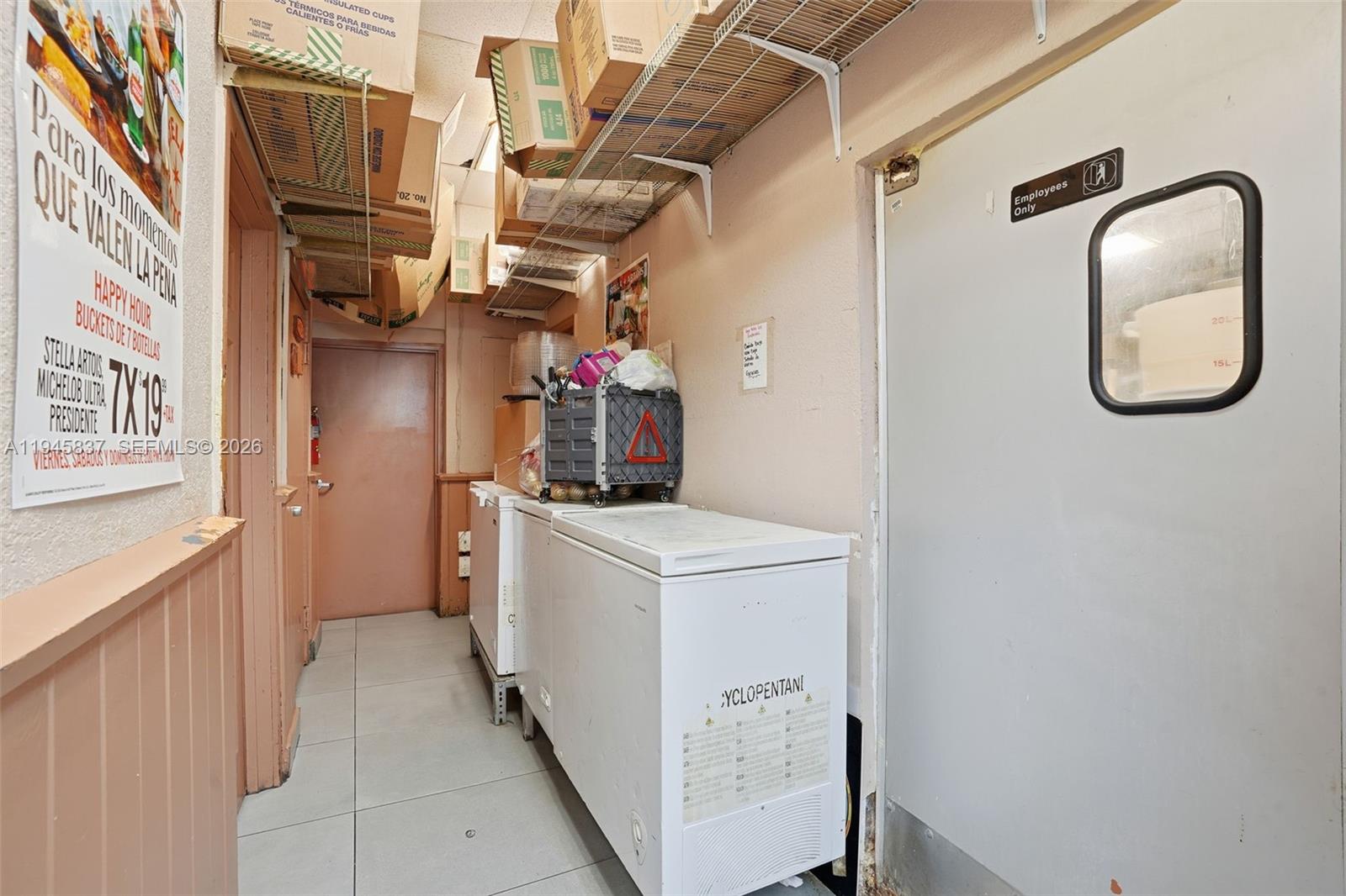 A narrow storage area features chest freezers, overhead wire shelving with boxes, and a door — Confidential 76th St, Hialeah FL 33018, HIALEAH, FL