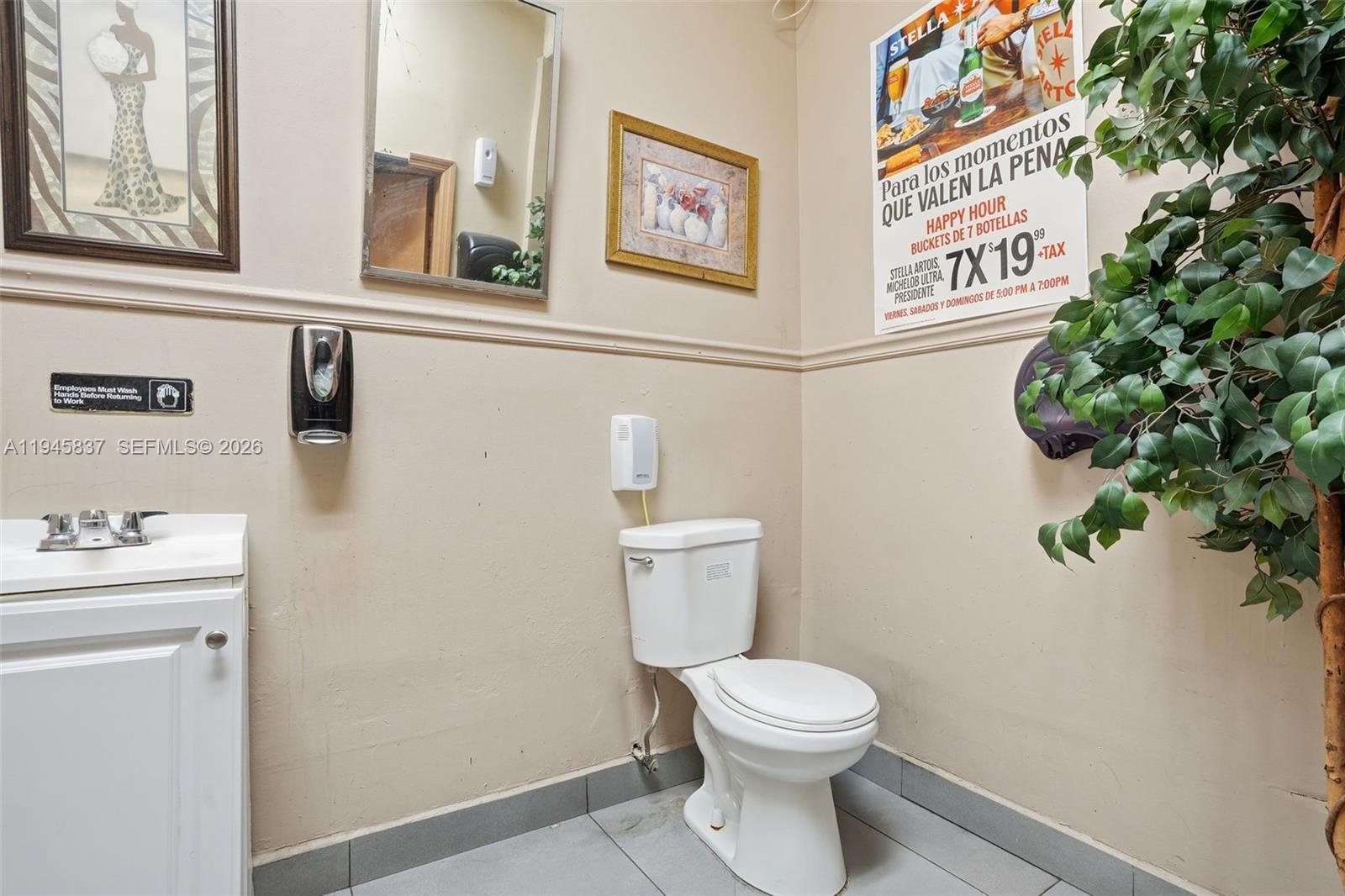 A small restroom features a white toilet, a vanity sink, and a wall-mounted beer advertisement — Confidential 76th St, Hialeah FL 33018, HIALEAH, FL