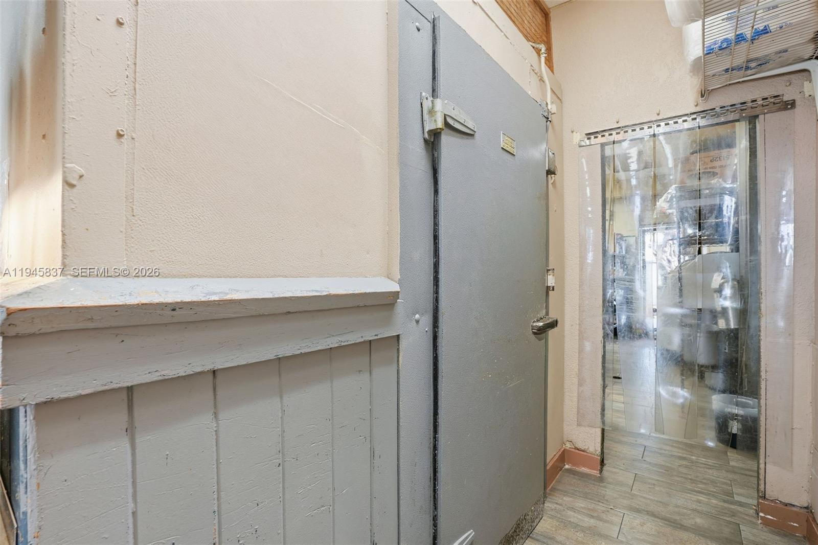 A gray industrial walk-in cooler door stands next to a plastic strip curtain doorway — Confidential 76th St, Hialeah FL 33018, HIALEAH, FL