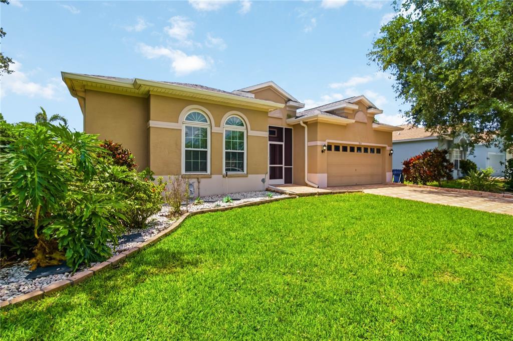 A tan single-story house with a two-car garage, arched windows, and a landscaped front yard — 5104 52ND AVENUE W, BRADENTON, FL