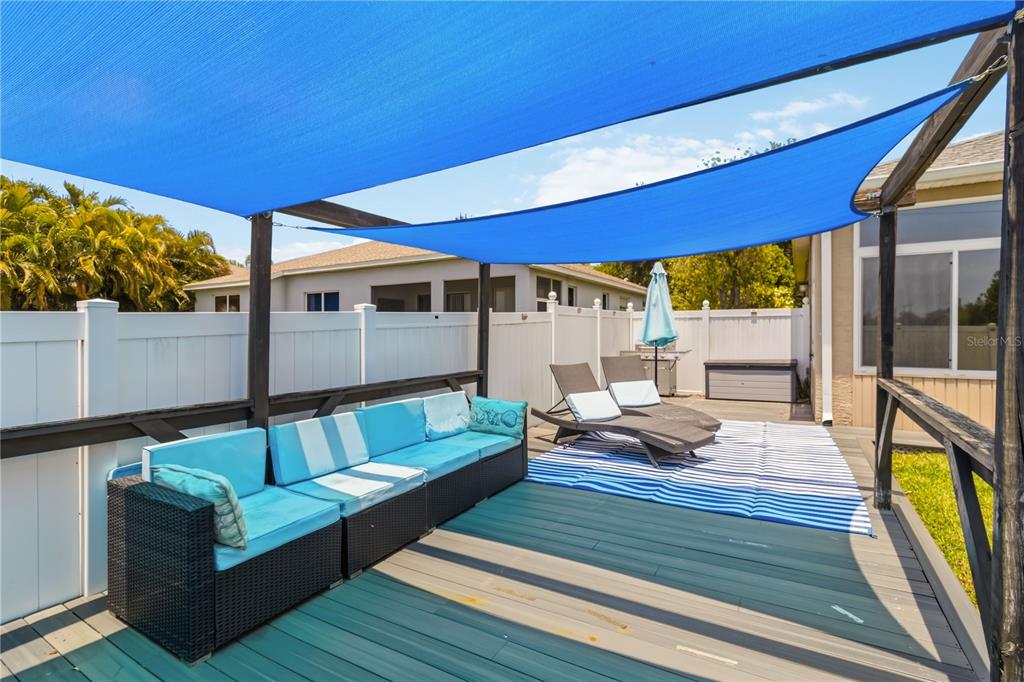 A backyard deck features a blue shade sail, wicker sectional seating, and two lounge chairs — 5104 52ND AVENUE W, BRADENTON, FL