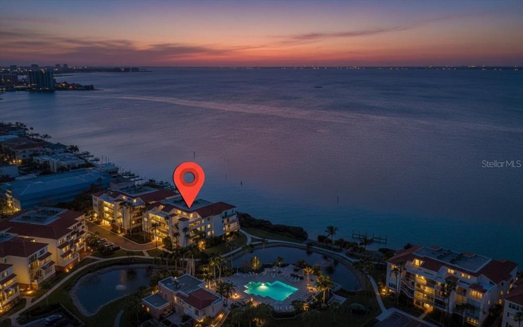 An aerial view shows a waterfront condominium complex at sunset with a red location pin — 380 GULF OF MEXICO DRIVE UNIT 515, LONGBOAT KEY, FL