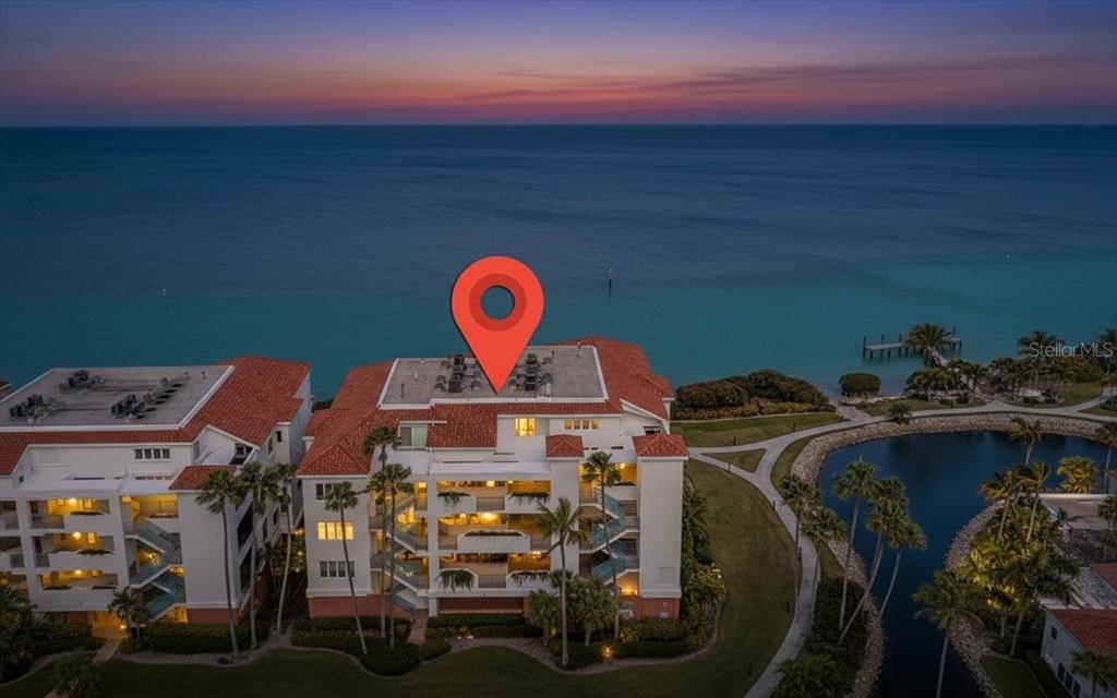 An aerial view shows a multi-story waterfront condominium building at dusk with a location pin — 380 GULF OF MEXICO DRIVE UNIT 515, LONGBOAT KEY, FL