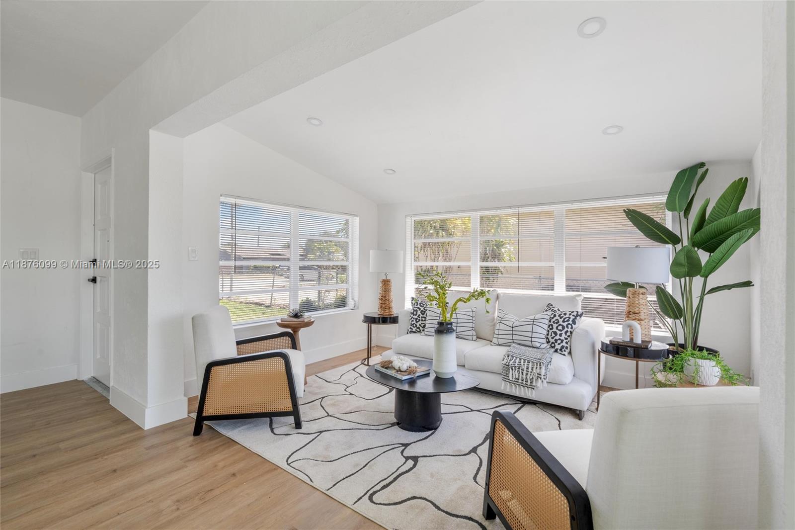 A bright living room features white walls, wood-look flooring, a patterned rug, and cane chairs — 3230 Taft St, Hollywood FL 33021, HOLLYWOOD, FL