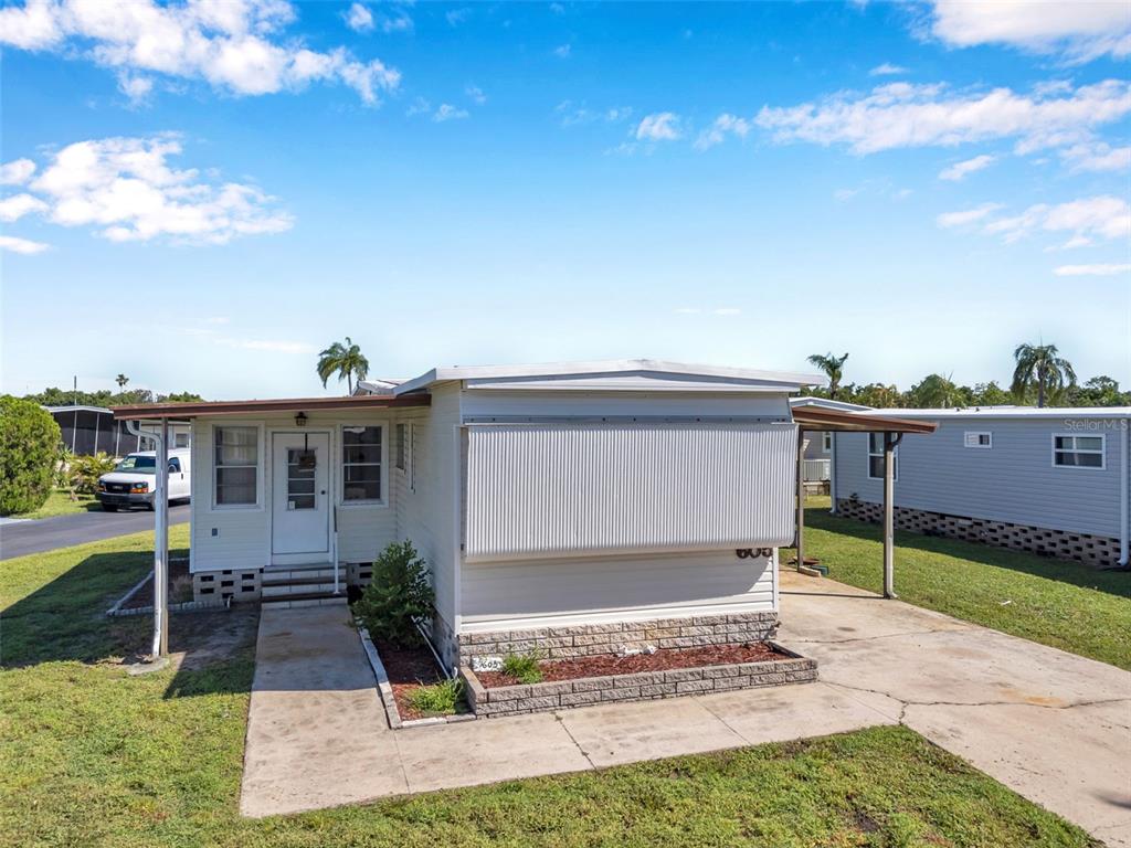 A single-story manufactured home features a metal awning, concrete driveway, and a small brick planter — 605 MOUNT LANCASTER AVENUE NE UNIT 634, ST PETERSBURG, FL