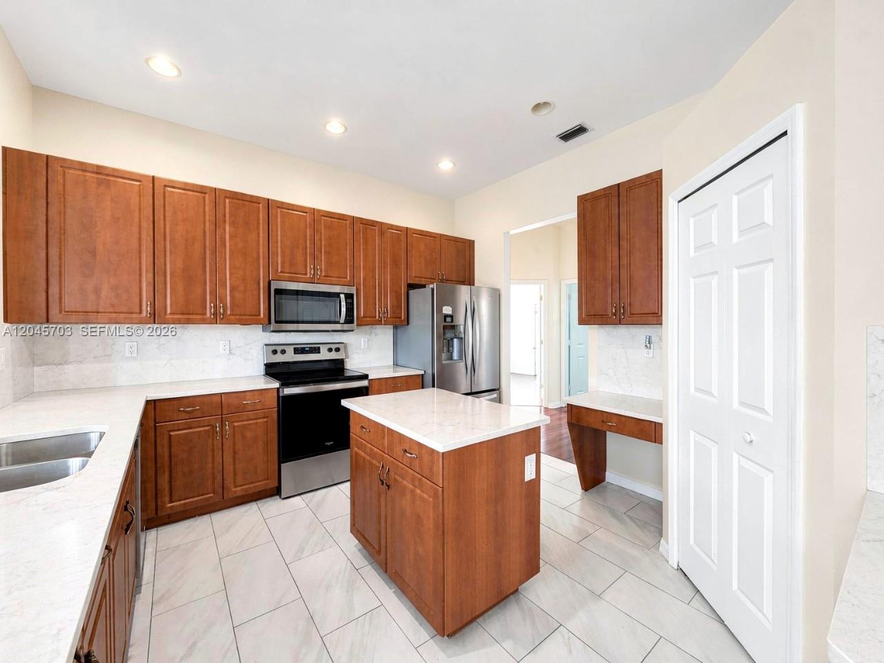 A kitchen features wood cabinets, stainless steel appliances, a center island, and white countertops — NAPLES, FL
