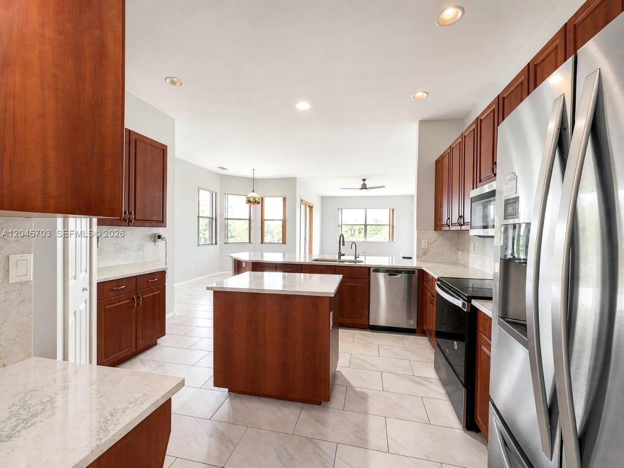 A kitchen features wood cabinets, stainless steel appliances, a center island, and light tile flooring — NAPLES, FL