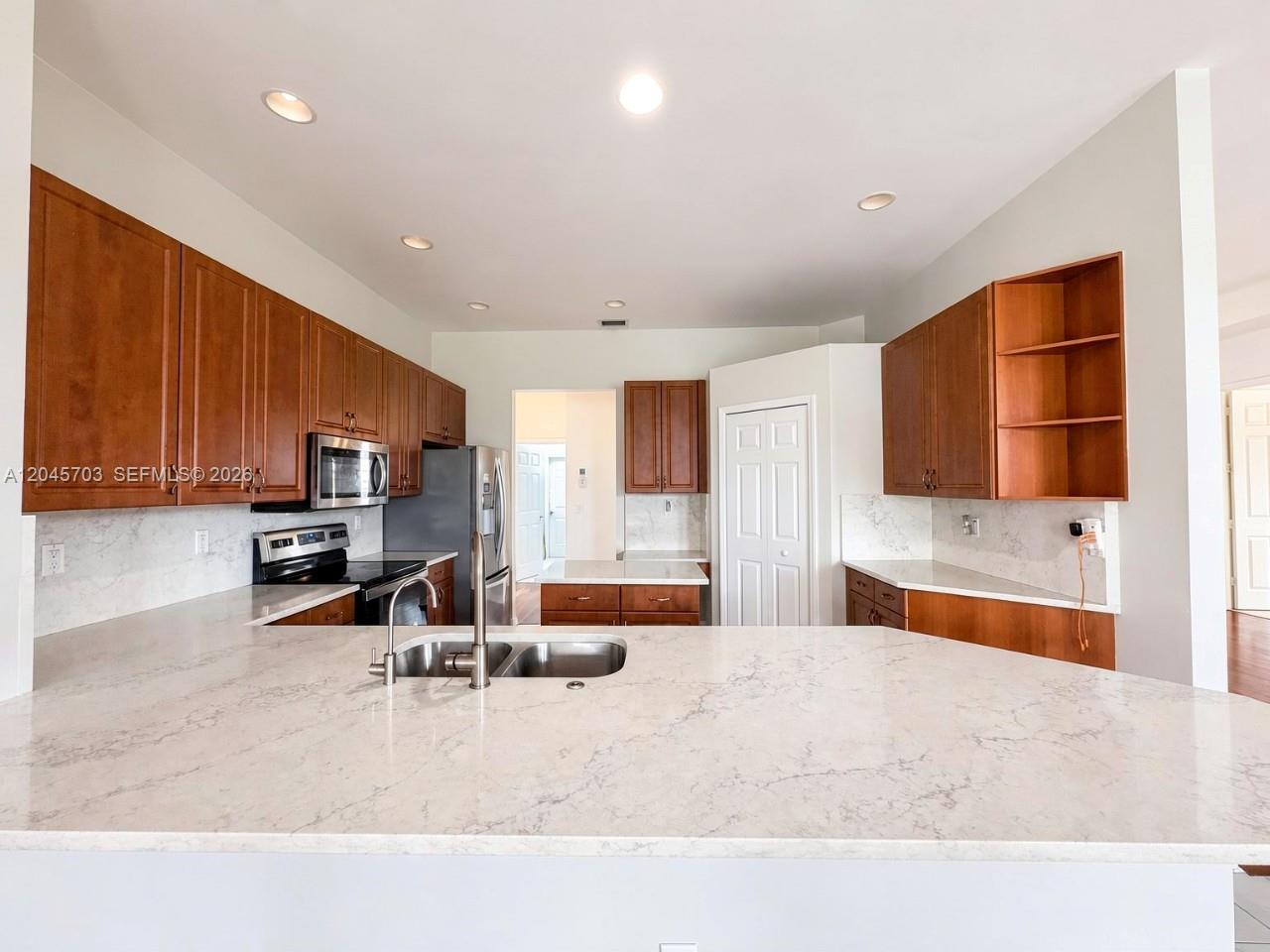 A kitchen features wood cabinets, white marble-patterned countertops, and a stainless steel sink — NAPLES, FL