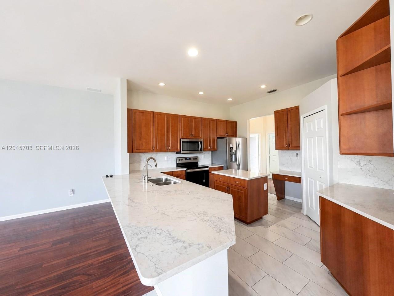 A kitchen features wood cabinets, white quartz countertops, stainless steel appliances, and tile flooring — NAPLES, FL