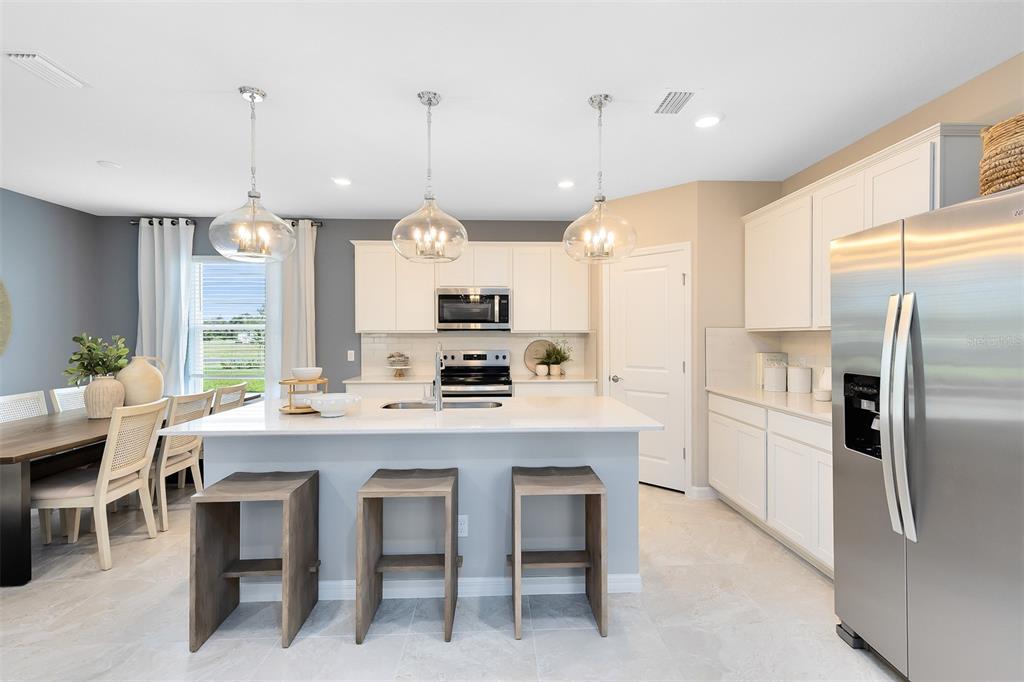 A modern kitchen features white cabinetry, a central island with bar stools, and stainless appliances — 6906 CREEK FALLS ALLEY, CLERMONT, FL