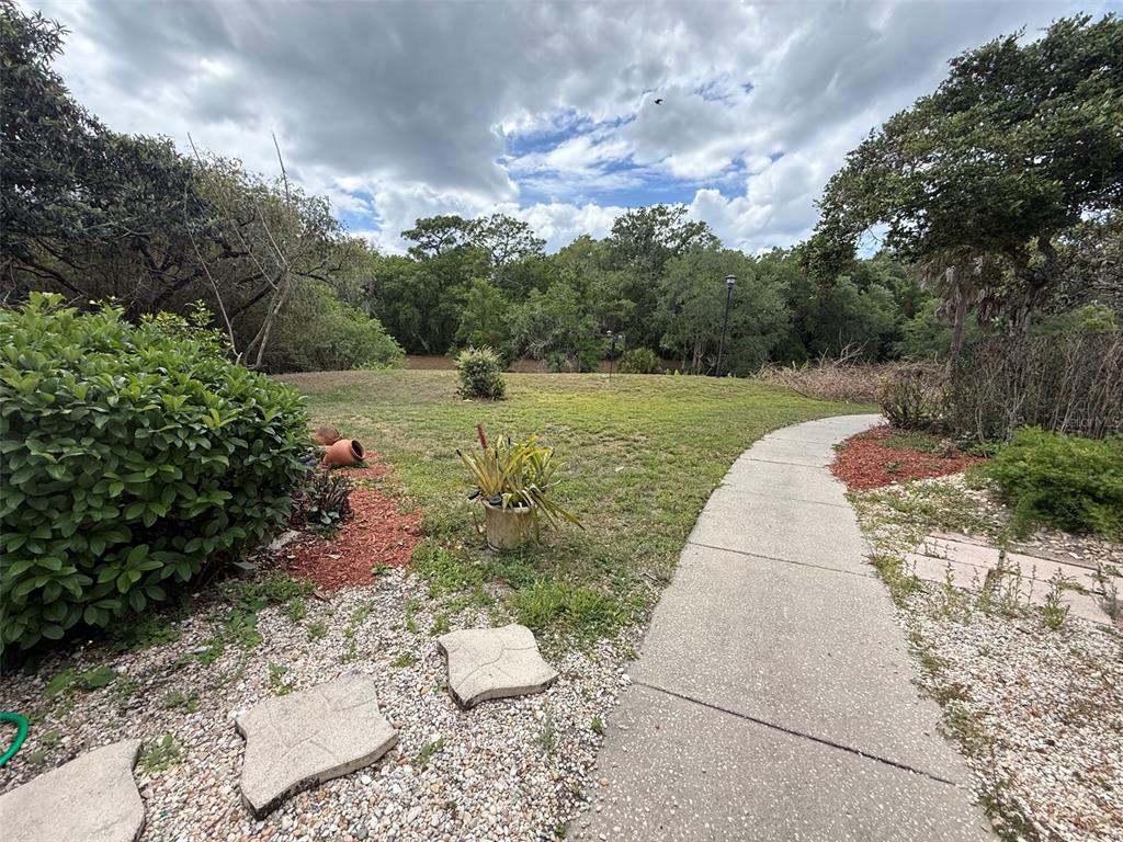 A concrete walkway leads through a grassy backyard toward a dense line of trees — 3940 ATRIUM DRIVE UNIT L7, ORLANDO, FL