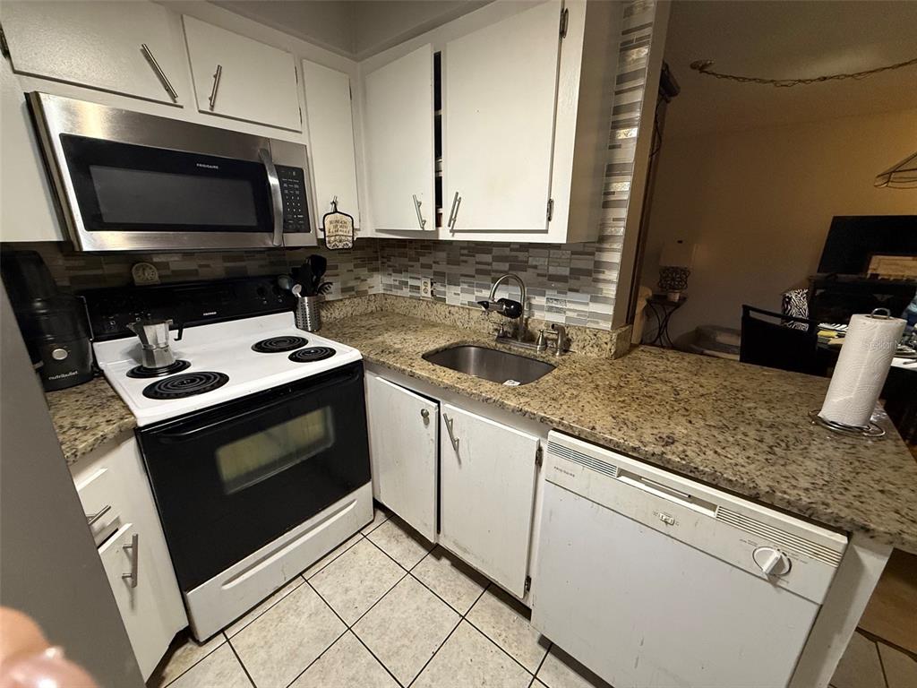 A kitchen features white cabinets, granite countertops, a stainless steel microwave, and white appliances — 3940 ATRIUM DRIVE UNIT L7, ORLANDO, FL