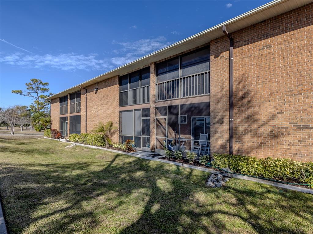 A two-story brick apartment building features screened-in balconies and patios overlooking a grassy lawn — 217 AIRPORT AVENUE W UNIT 216, VENICE, FL