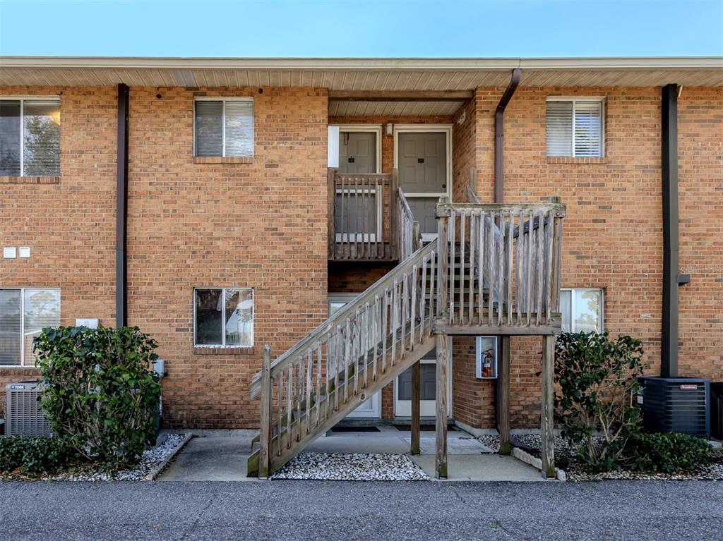 An exterior view of a two-story brick apartment building with an outdoor wooden staircase — 217 AIRPORT AVENUE W UNIT 216, VENICE, FL