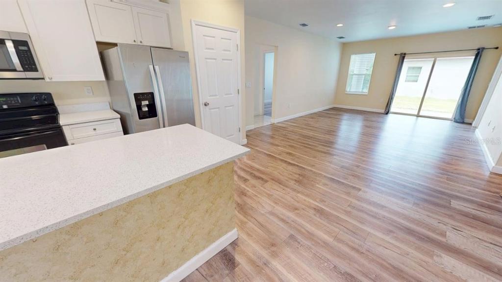 A kitchen with white cabinets and stainless steel appliances opens into a spacious living area — 6217 JASON STREET UNIT 1, ORLANDO, FL