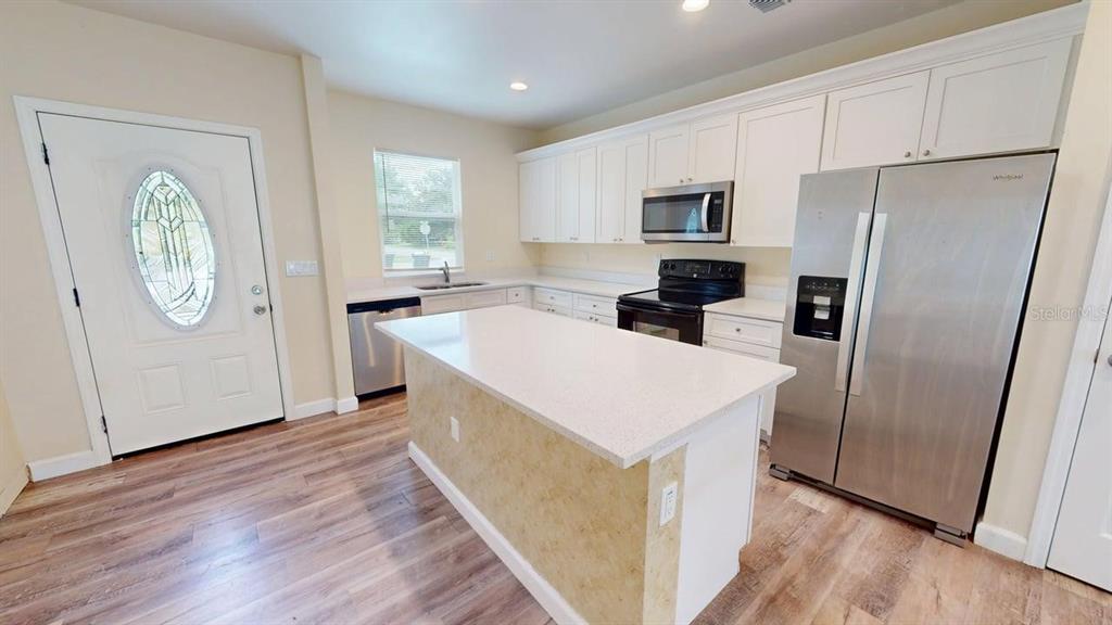 A kitchen features white cabinets, stainless steel appliances, a central island, and wood-look flooring — 6217 JASON STREET UNIT 1, ORLANDO, FL
