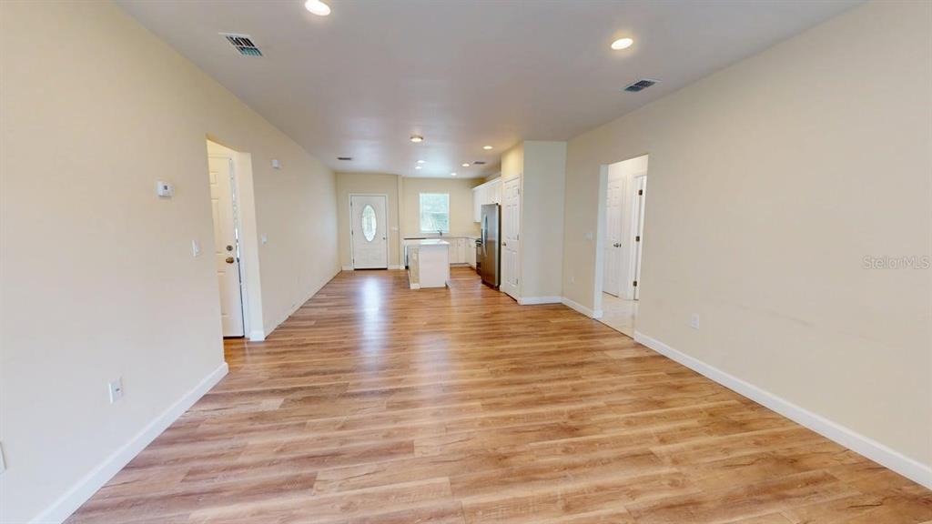 An open-concept living area features light wood-look flooring, recessed lighting, and a kitchen beyond — 6217 JASON STREET UNIT 1, ORLANDO, FL