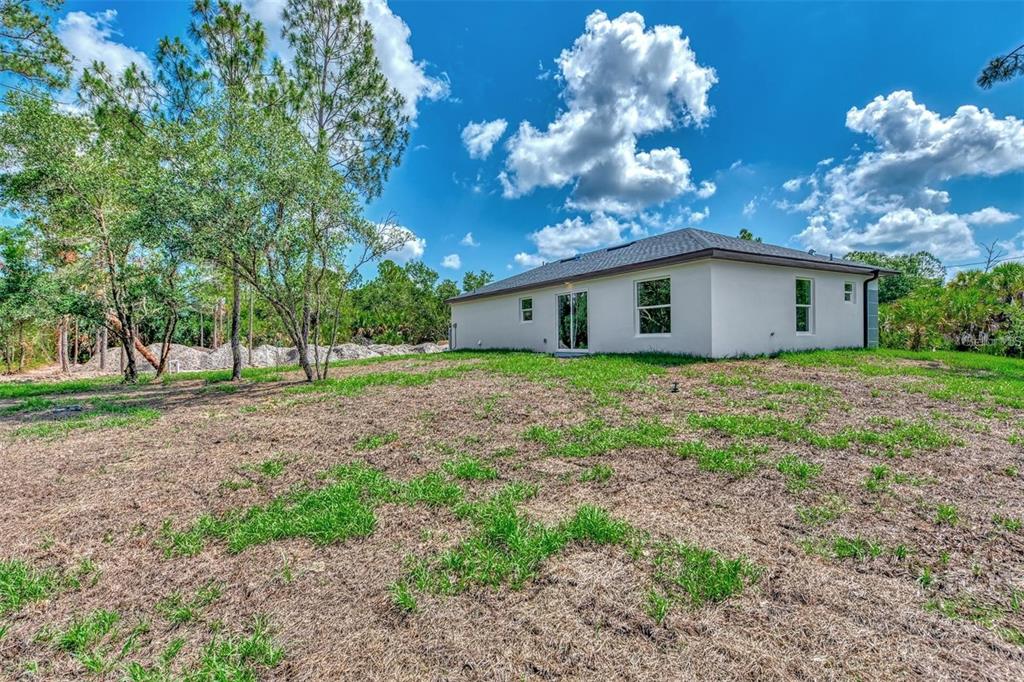 The exterior rear view of a single-story house with a yard and surrounding trees — 4637 CORBETT LANE, NORTH PORT, FL