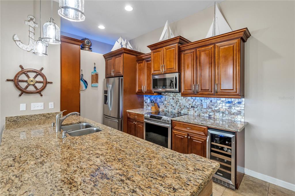 A kitchen features wood cabinets, granite countertops, a tile backsplash, and nautical-themed wall decor — 6420 BANYAN BOULEVARD UNIT 303, NEW PORT RICHEY, FL