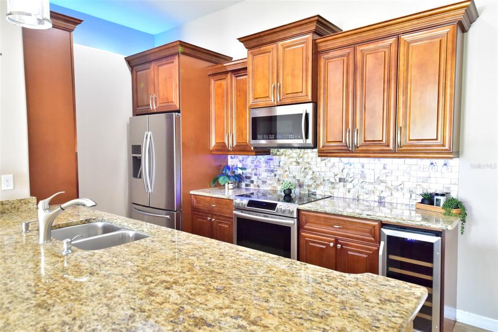 A kitchen features wood cabinets, granite countertops, stainless steel appliances, and a tiled backsplash — 6420 BANYAN BOULEVARD UNIT 303, NEW PORT RICHEY, FL