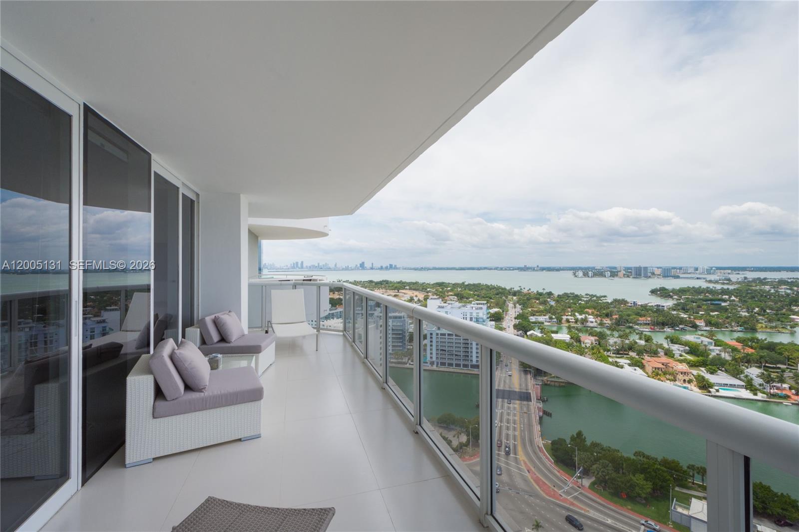 A high-rise balcony features white wicker furniture and a glass railing overlooking a coastal city — 6301 Collins Ave # 3006, Miami Beach FL 33141, MIAMI BEACH, FL