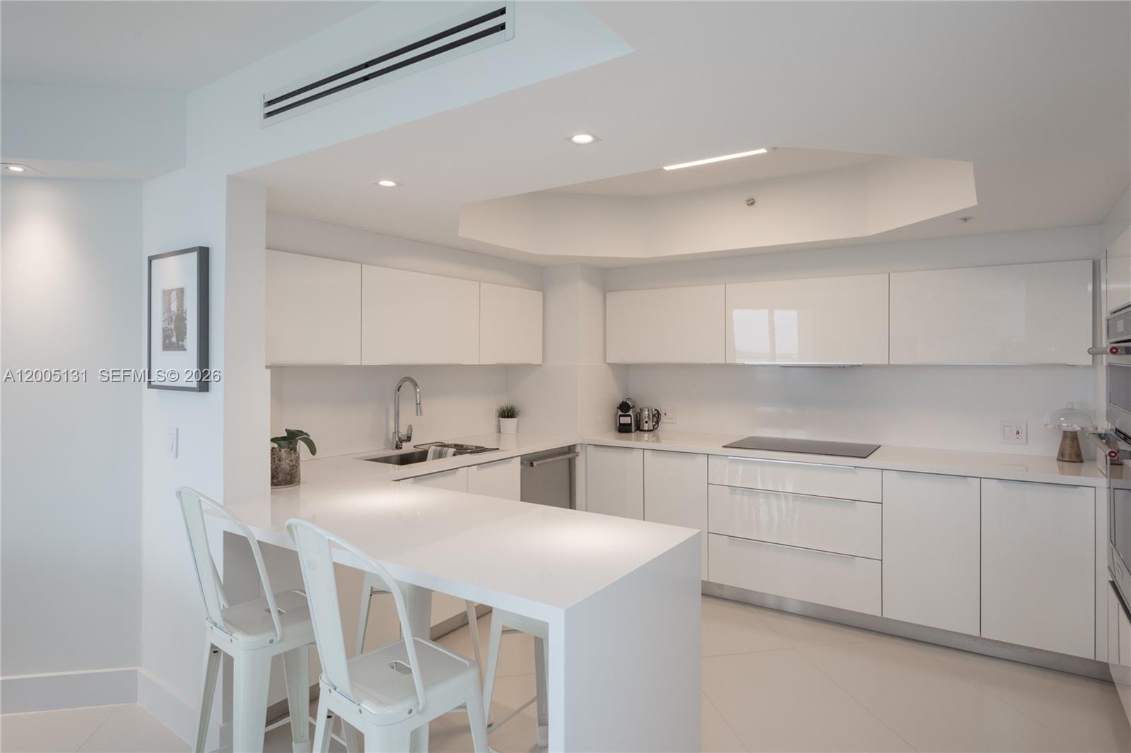 A modern, all-white kitchen features flat-panel cabinetry, quartz countertops, and a breakfast bar — 6301 Collins Ave # 3006, Miami Beach FL 33141, MIAMI BEACH, FL