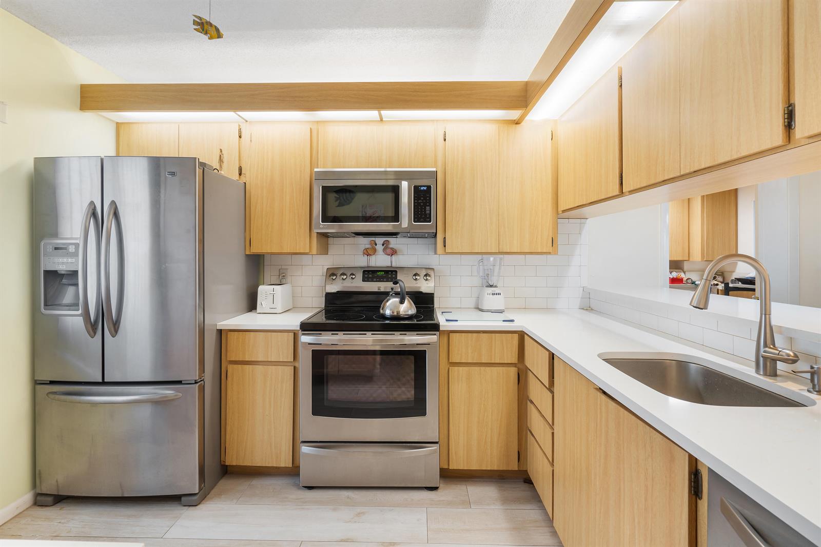 A kitchen features light wood cabinets, stainless steel appliances, white countertops, and a subway tile backsplash — 901 Seafarer Circle # 306, Jupiter FL 33477, JUPITER, FL