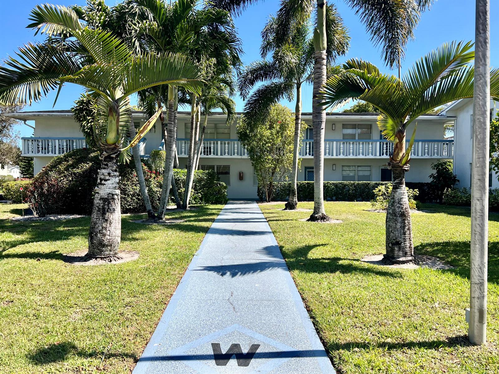 A blue walkway leads toward a two-story apartment building surrounded by palm trees and grass — 635 Durham W, Deerfield Beach FL 33442, DEERFIELD BEACH, FL