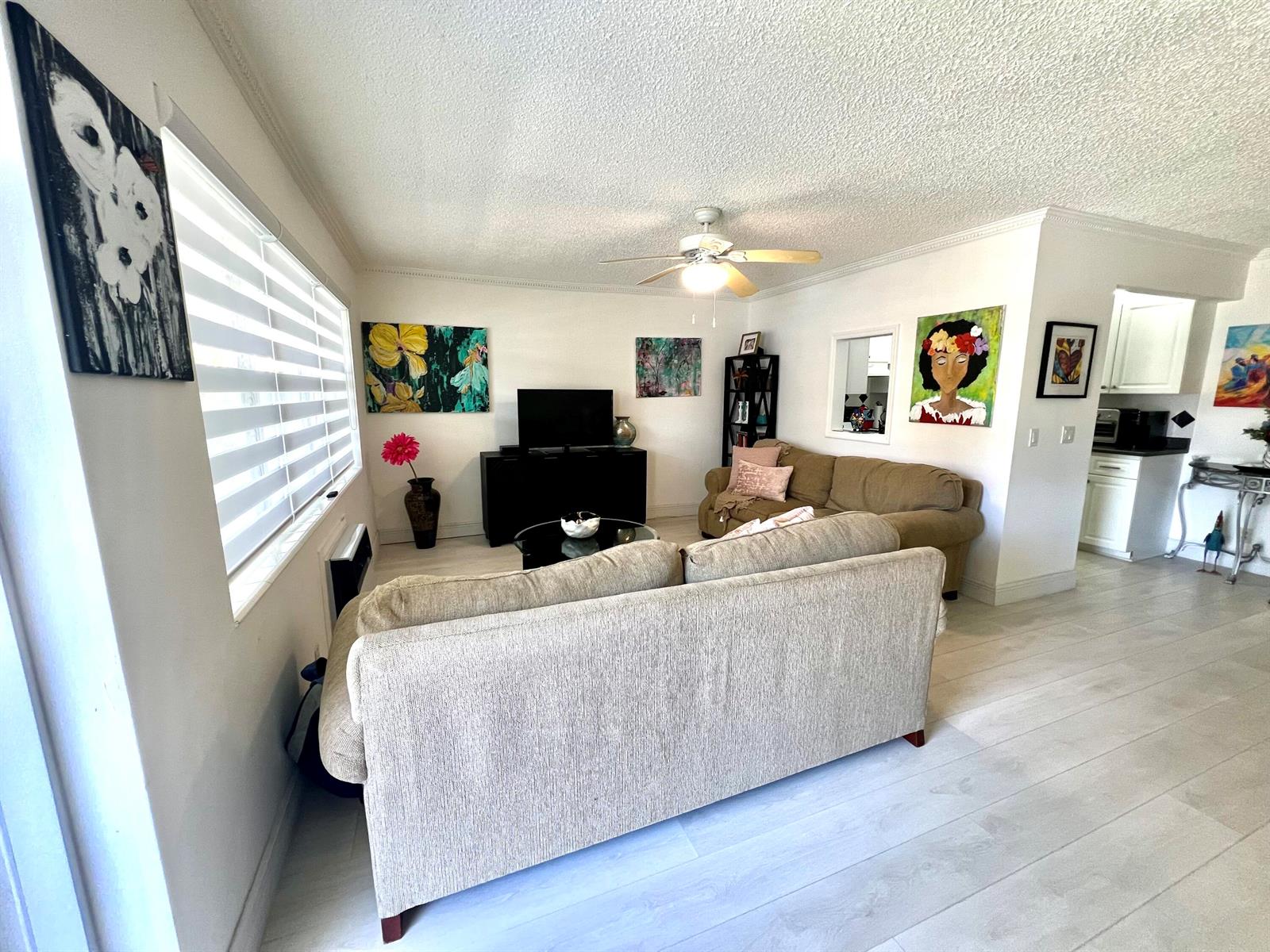 A living room features two beige sofas, a television on a black stand, and artwork — 635 Durham W, Deerfield Beach FL 33442, DEERFIELD BEACH, FL
