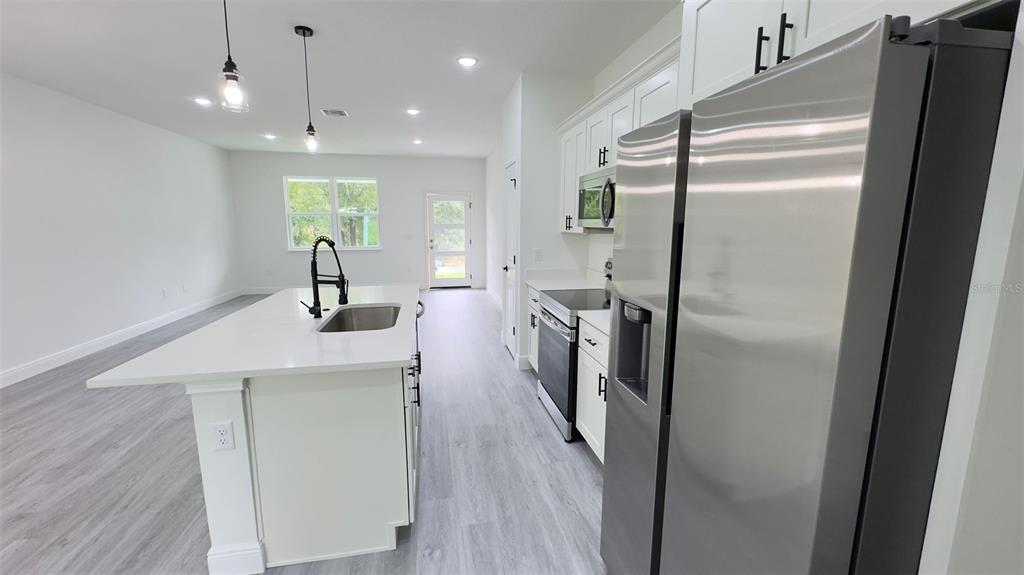 A modern kitchen features a white island with a sink, stainless appliances, and light flooring — 2827 W XENOX DRIVE, CITRUS SPRINGS, FL