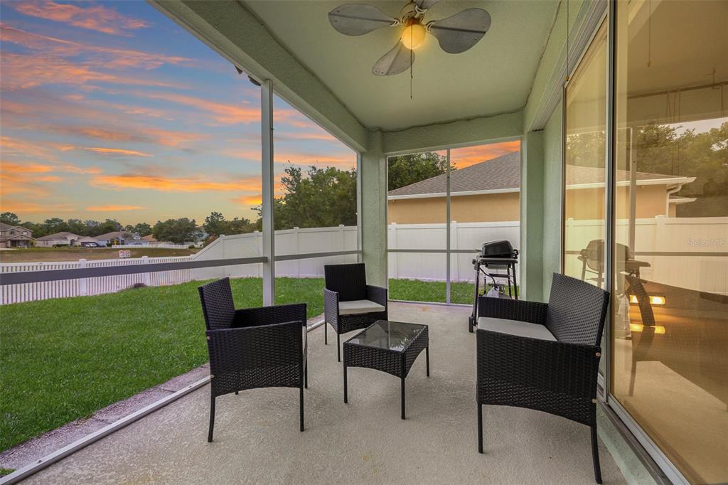 A screened-in patio features wicker furniture, a ceiling fan, and a view of the backyard — 4215 MAPLEHURST WAY, SPRING HILL, FL