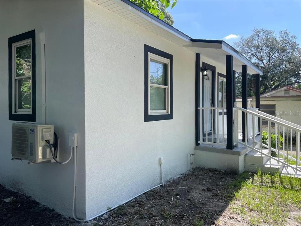 A white stucco house exterior features black window trim, a covered porch, and an AC unit — 1812 E OKALOOSA AVENUE, TAMPA, FL