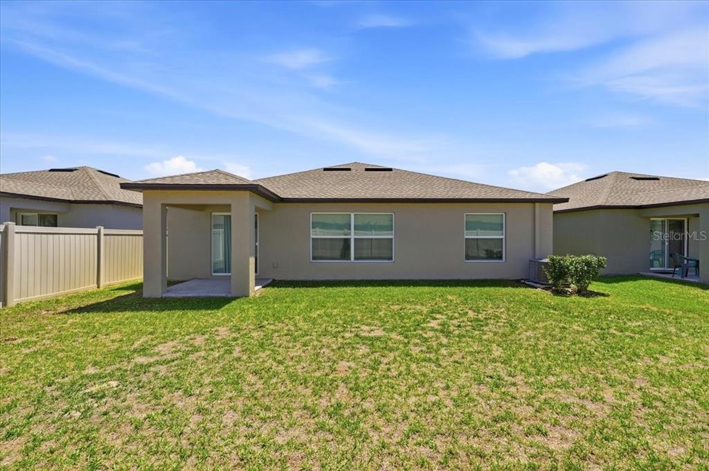The exterior rear view of a single-story house features a covered patio and lawn — 35029 BRACKETT BEND, ZEPHYRHILLS, FL