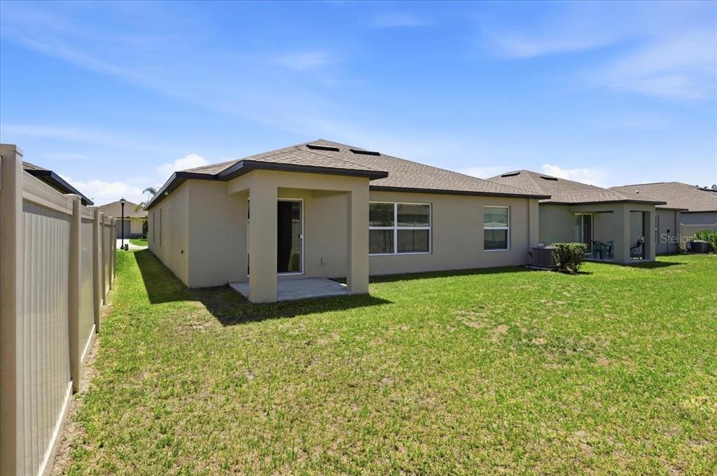 The exterior rear view of a tan house features a covered patio and vinyl fencing — 35029 BRACKETT BEND, ZEPHYRHILLS, FL