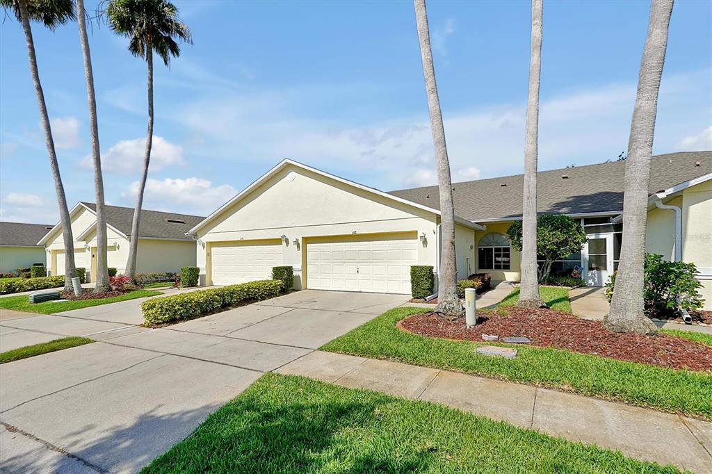 A view of the exterior of a light-colored duplex home with two garages and palm trees — 168 CLUB VILLAS LANE, KISSIMMEE, FL
