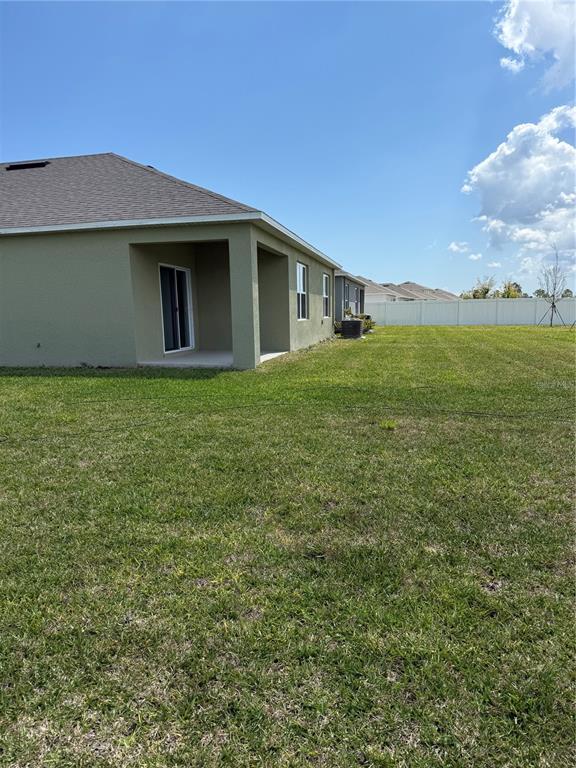 The exterior of a tan house features a covered patio and a large grassy backyard — 2665 NEVERLAND DRIVE, NEW SMYRNA BEACH, FL
