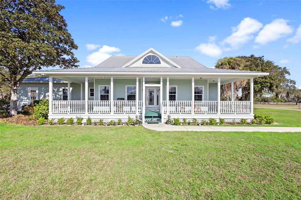 A light green, single-story house with a metal roof and a wide, wrap-around front porch — 42554 MAGGIE JONES ROAD, PAISLEY, FL