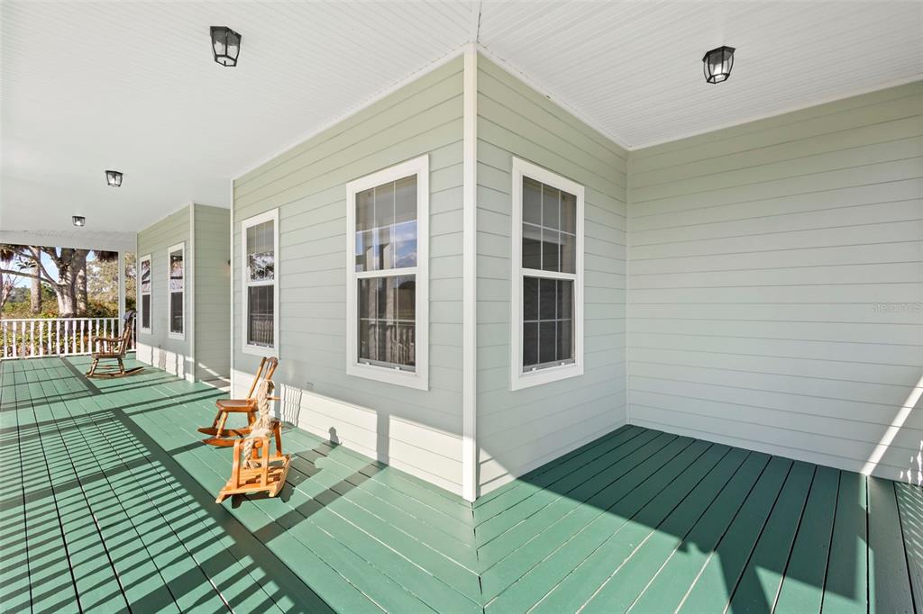 A wide, covered porch with green wooden decking and several rocking chairs along the exterior wall — 42554 MAGGIE JONES ROAD, PAISLEY, FL