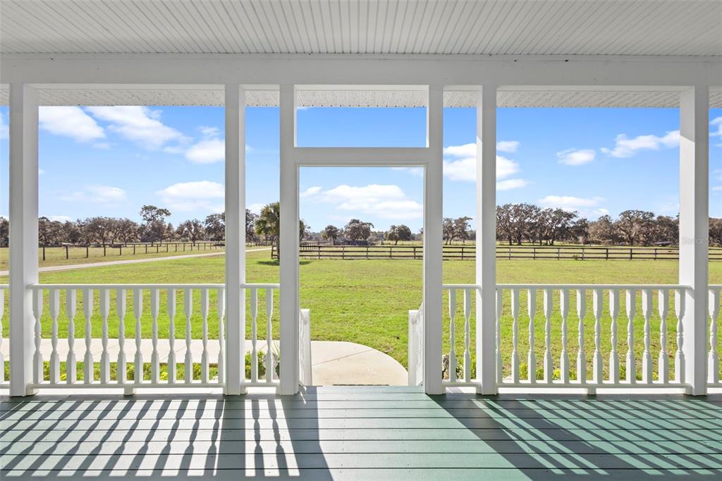 A covered porch with white railings overlooks a grassy field and a fenced pasture — 42554 MAGGIE JONES ROAD, PAISLEY, FL