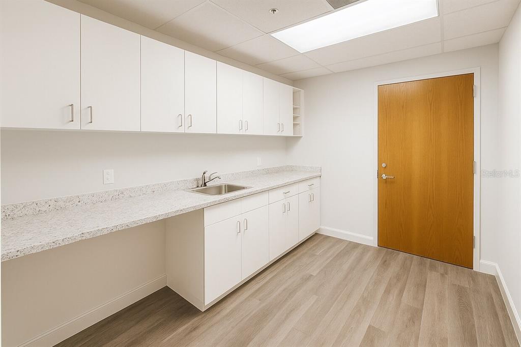 A room with white cabinets, a sink, a speckled countertop, and a wooden door — 14100 FIVAY ROAD UNIT 120, HUDSON, FL