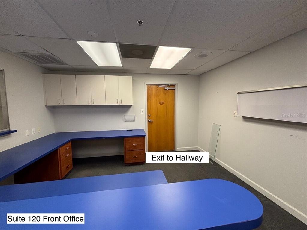 An office space features blue L-shaped desks, white upper cabinets, and a wooden exit door — 14100 FIVAY ROAD UNIT 120, HUDSON, FL