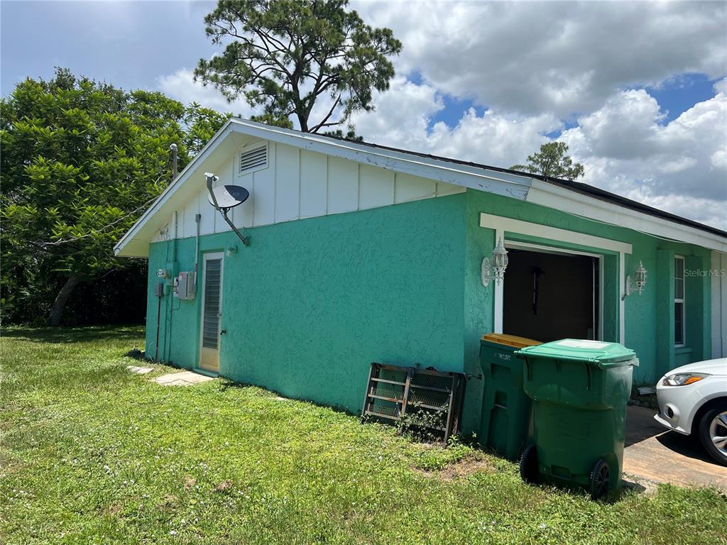 The exterior of a teal-colored house features a garage, a side door, and trash bins — 644 ERROLL STREET, PORT CHARLOTTE, FL