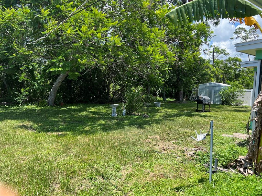 A grassy backyard features a birdbath, a small storage shed, and a charcoal grill — 644 ERROLL STREET, PORT CHARLOTTE, FL
