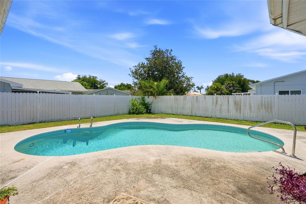 A kidney-shaped swimming pool sits in a backyard enclosed by a white privacy fence — 13219 RIDGE ROAD, LARGO, FL